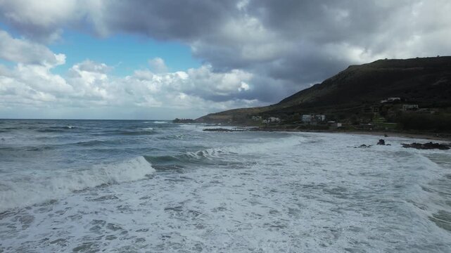 Flight over surf toward a rocky coast under dramatic clouds - Crete