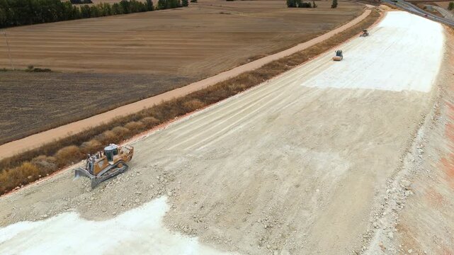 An aerial view of a yellow bulldozer leveling ground alongside a motor grader on a highway construction site