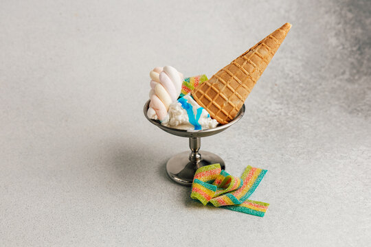 Ice cream served in a silver bowl with a cone and colorful decoration on a light surface