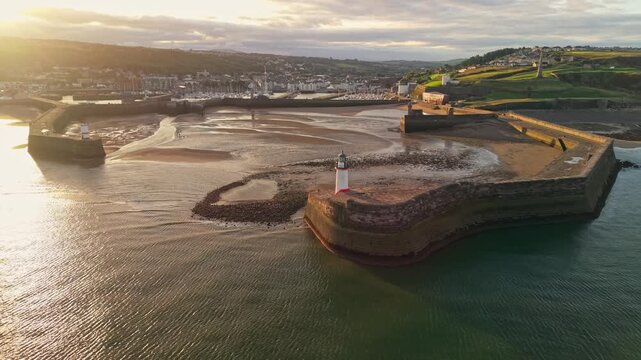 Aerial panoramic views of Whitehaven coastal town and civil parish. Lighthouse demonstration looking to the Irish sea in Sunrise, golden hour. Drone POV exploration of Devon County, England, UK.