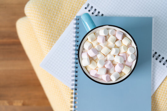 Top view blue ceramic mug of hot cocoa with marshmallows and a folded yellow blanket on a wooden bench