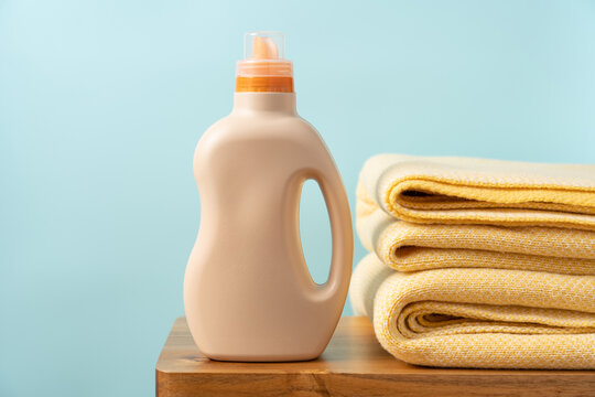 Yellow blankets and laundry detergent bottle on a wooden bench against a blue background, clean laundry and textile care concept