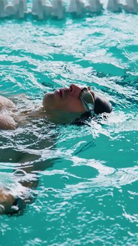 Swimmer glides on backstroke through clear pool water. Water ripples around focused athlete. Ideal for fitness, training, or athletic montage clips