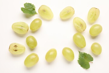 Fototapeta premium Fresh ripe grapes and green leaves on white background, flat lay. Space for text