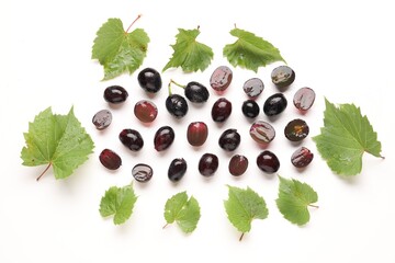 Fototapeta premium Fresh ripe grapes and green leaves on white background, flat lay