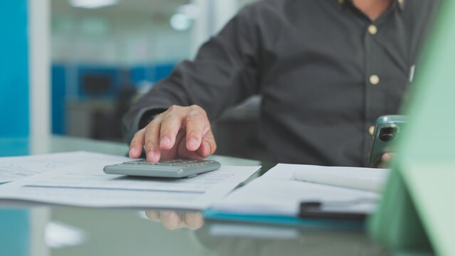 Accountant presses keys on calculator review financial paper report holding smartphone desk workspace office background indoor setting.