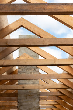 Wooden roof rafters constructing a house framework with a concrete chimney, building a future home and showing the progress of a construction project against a blue sky
