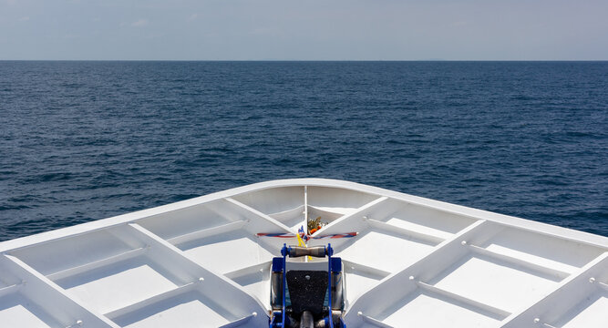The white bow of a ferry cruises steadily across the deep blue ocean towards the distant horizon under a clear sky in Thailand.