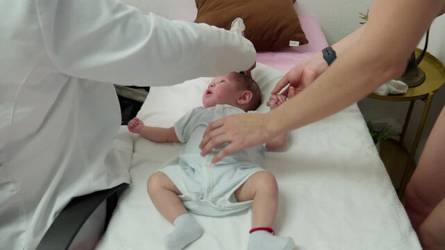 A medical professional performs a cranial ultrasound screening on a newborn infant lying on an exam table while the mother stays close by in a clinic in Mexico.