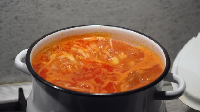 Traditional shchi cabbage soup cooking process with fresh shredded vegetables inside a hot boiling enamel pot indoors. Homemade eastern european recipe cuisine preparation scene, rustic kitchen. 