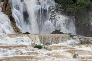 Kuang Si Waterfall cascades over limestone tiers into blue-green pools surrounded by lush tropical jungle forest. © Eugene Ga