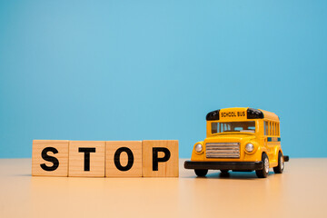 Wooden letter blocks spelling STOP beside a miniature yellow school bus on a beige surface against a blue background. School bus safety, traffic awareness. © Akmalism Photography