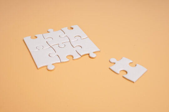 Partially assembled white jigsaw puzzle with loose pieces on a beige background. Concept of missing information, incomplete solutions, problem solving and finding the right connection.