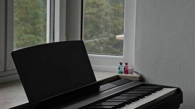 Digital Piano Keyboard By A Window On A Grey Rainy Morning With Blurred Wet Greenery Outside