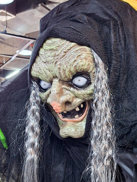 scary old witch face prop with green wrinkled skin grey hair and black hood halloween horror decoration