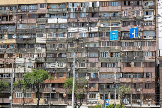 Weathered facade of a soviet era apartment building crowded with mismatched balconies and crisscrossed by tangled electric wires above a street sign, Yerevan, Armenia