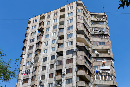 Low angle corner view of a soviet era apartment tower with rows of weathered balconies hung with drying laundry rising against a clear blue sky, Yerevan, Armenia