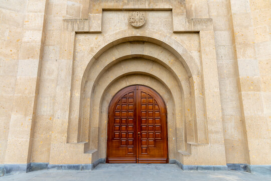 Carved wooden double doors with rosette ornament and geometric panels are set beneath layered stone arches at Saint Gregory the Illuminator Cathedral, Yerevan, Armenia