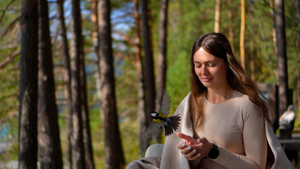 Beautiful moment of a gentle female tourist letting a wild great tit bird fly away from her palms in a scenic coniferous forest. © OlTarakanov