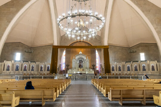 A large wheel shaped chandelier hangs above the nave altar and pews inside Saint Gregory the Illuminator Cathedral beneath a vaulted stone ceiling, Yerevan, Armenia