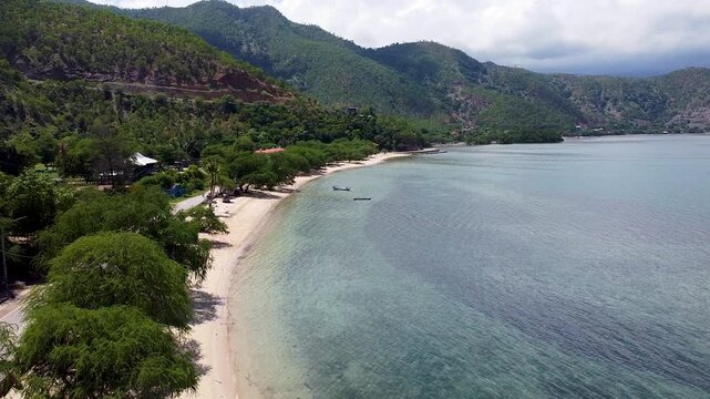 Aerial view rising above coastal landscape of Metiaut in Dili, Timor-Leste with white sandy beaches, crystal clear ocean, rugged hilly terrain in Southeast Asia