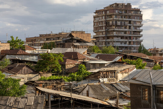 Rusty corrugated rooftops of the old town cluttered with antennas and satellite dishes stretching toward a tall concrete Soviet era apartment tower behind, Yerevan, Armenia