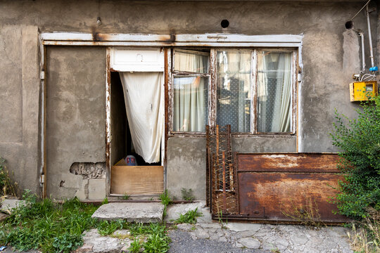 Old decayed doorway and window of a weathered house facade covered with peeling plaster a faded curtain a rusty sheet of corrugated metal and tangled wire, Yerevan, Armenia