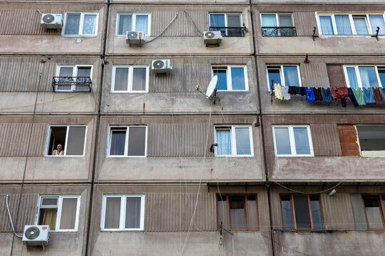 Weathered facade of a Soviet era apartment building covered with air conditioners laundry and satellite dishes while a man looks out of a window, Yerevan, Armenia