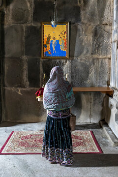 A woman seen from behind kneels in prayer before a religious icon and flickering candles inside the medieval Haghpat Monastery an Armenian heritage site, Haghpat, Armenia