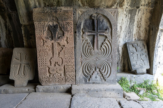 Ornate khachkar stone crosses covered in lichen lean against a weathered wall in the outdoor grounds of the medieval Haghpat Monastery heritage site, Haghpat, Armenia