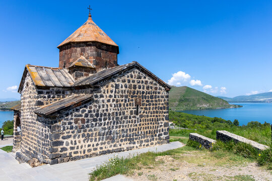 Surp Astvatsatsin church seen from a hillside path lined with ancient stone walls overlooking the scenic waters of Lake Sevan and surrounding highland hills, Sevanavank, Armenia