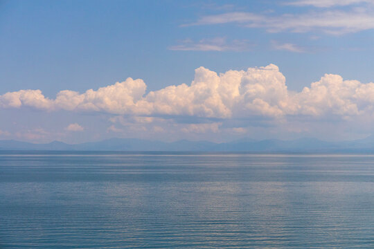 Cumulus clouds drift above the calm tranquil waters of the lake beneath a wide blue sky creating a peaceful panoramic highland view in Gegharkunik Province, Sevan, Armenia