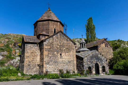 Stone church of the ancient monastery features a conical dome and bell tower rising above the hill under a cloudy sky in Gegharkunik Province, Artsvanist, Armenia