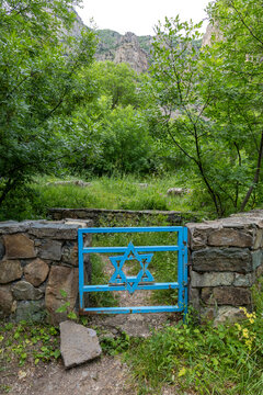 Blue metal gate decorated with a Star of David marks the entrance to an ancient Jewish cemetery set among forested mountains and rocky terrain, Eghegis, Armenia