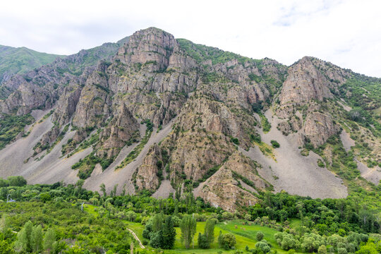Rugged rocky mountain peak rises above a green forested valley with steep cliffs and ridges stretching across a remote highland panorama under open sky, Eghegis, Armenia