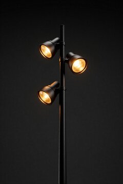 Modern black street lamp post with three glowing warm lights. Triple spotlight fixture stands against dark background. Industrial outdoor lighting design provides bright illumination for urban night