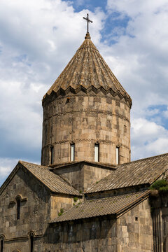 A close up of the stone bell tower and iron cross of Tatev Monastery stands out sharply against the forested green mountains in the distant background, Tatev, Armenia