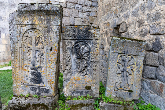 Three ornately carved Armenian khachkar cross stones stand displayed on the weathered lichen covered wall of the historic Saint Pogos and Petros church, Tatev, Armenia