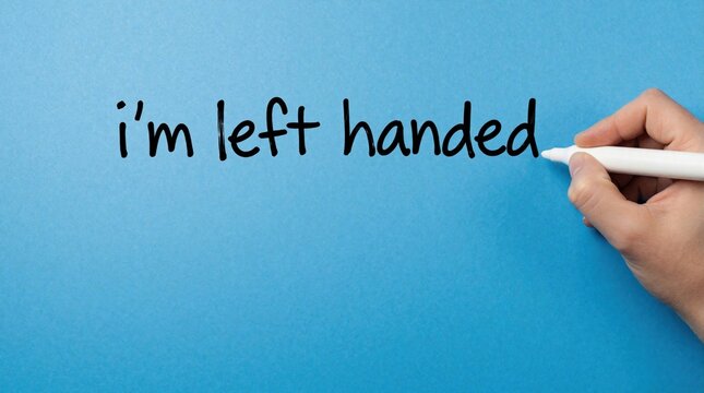 Left handed person writes text on blue background using white marker. Human hand holds pen to write i left handed message. Simple message about leftie lifestyle dexterity concept on solid blue wall.