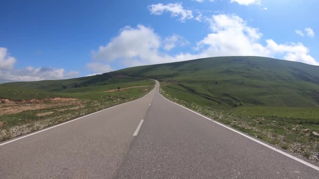 Vehicle driving along scenic mountain road through lush green landscapes under bright blue sky during summer travel adventure.