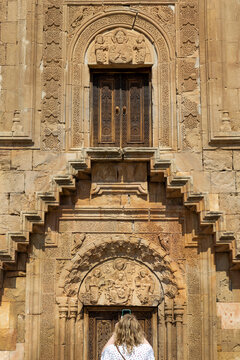 Lone visitor in a dress standing before the carved tympanum entrance depicting the Madonna and Christ child at Astvatsatsin church and monastery, Noravank, Armenia