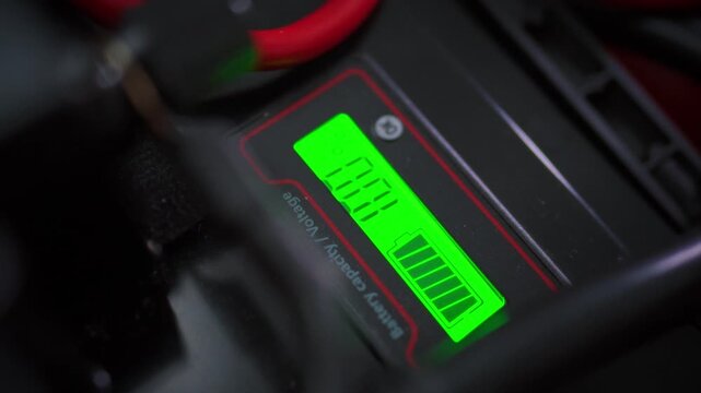 A battery charge indicator showing 100 percent captured in close-up against power cables and backup power equipment. Concept of complete solar battery charge and home energy independence