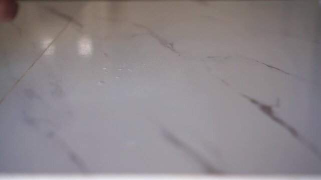 Hand spritzing cleaner onto a marble table surface before wiping. Cleaning footage capturing sanitation, housework, and domestic routine.