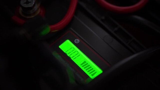 A digital display shows 100 percent battery charge on the interface, surrounded by heavy power cables and units, representing the concept of stored solar energy