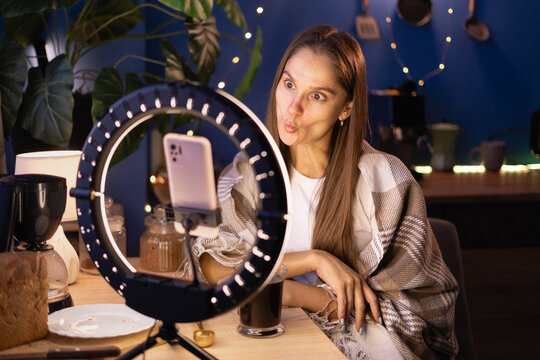 Goofy Woman influencer covering warm blanket making fish face lips films video content for social media using phone with ring light at home, live streaming. vlog tutorial