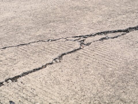 Close up view of a cracked and damaged concrete road surface showing structural wear, destruction, and fault lines. Ideal for industrial, construction, and infrastructure background 