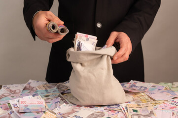 adult man holds textile pouch filled with Ukrainian hryvnia cash bills. corrupt politician hides illegal money payout above table. investor manages secret budget, bribe savings, capital. © Olena Vasylieva