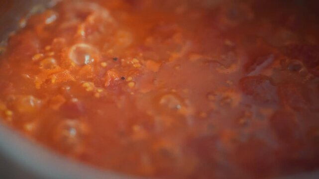 Bubbling tomato sauce with visible pulp and chunks in a metal pot on the stove. Top view close-up. Concept of homemade tomato sauce cooking and traditional pizza base preparation
