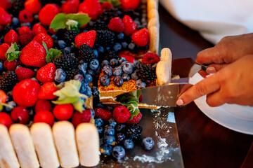 Hands slicing fresh berry cake topped with strawberries and blueberries © 9parusnikov