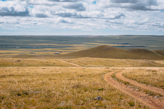Dirt track winding through the vast Mongolian steppe under a dramatic cloudy sky.